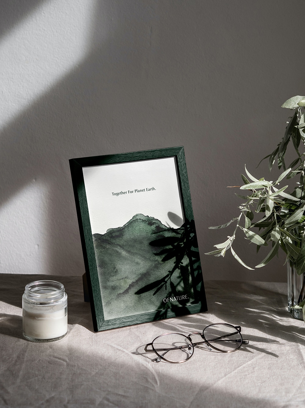 Framed OF NATURE landscape artwork on a sunlit table