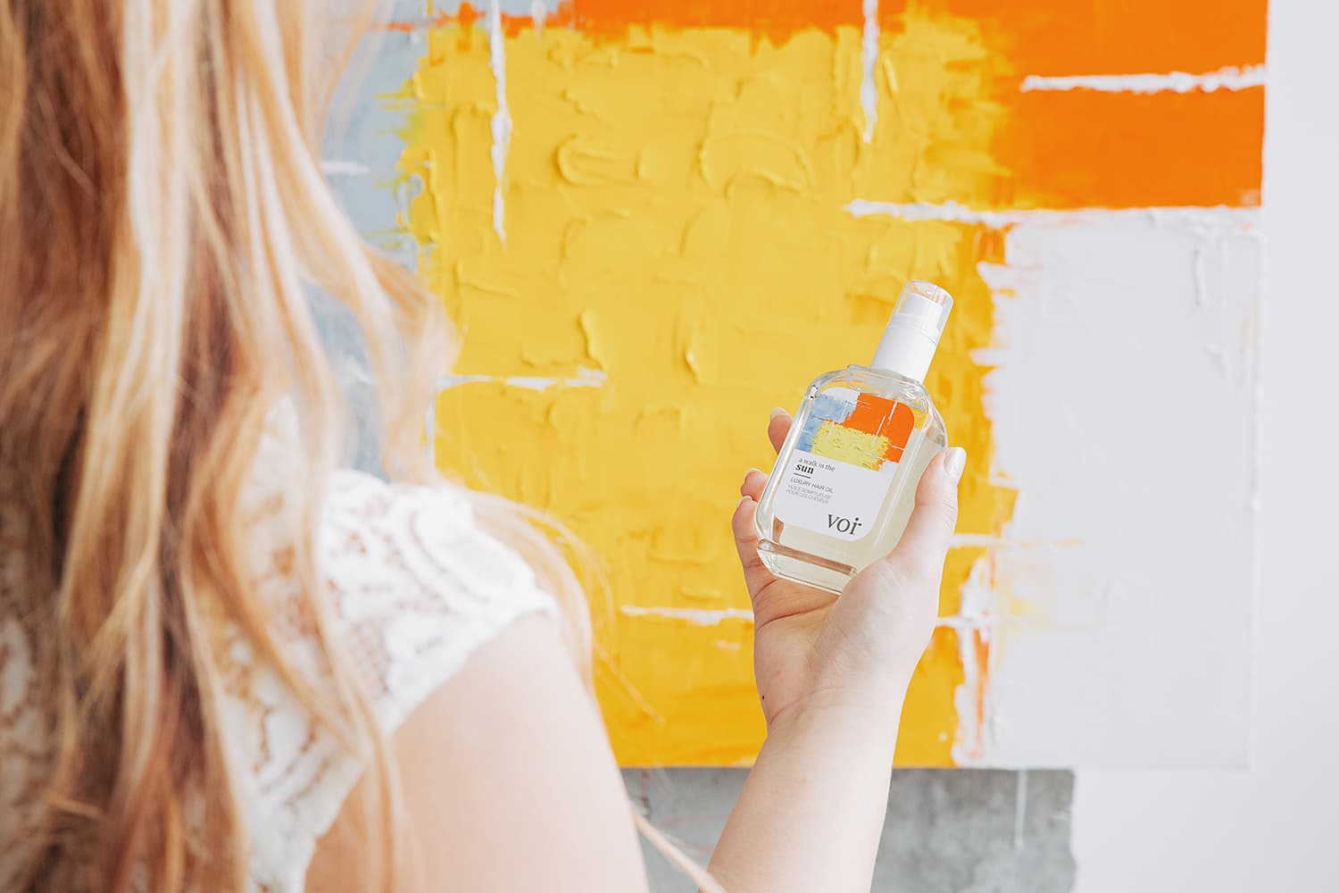 VOIR hair oil held against a yellow and orange painted backdrop